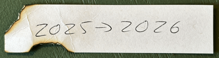 Photo of singed and twisted scrap of paper with 2025 > 2026 written in pen.