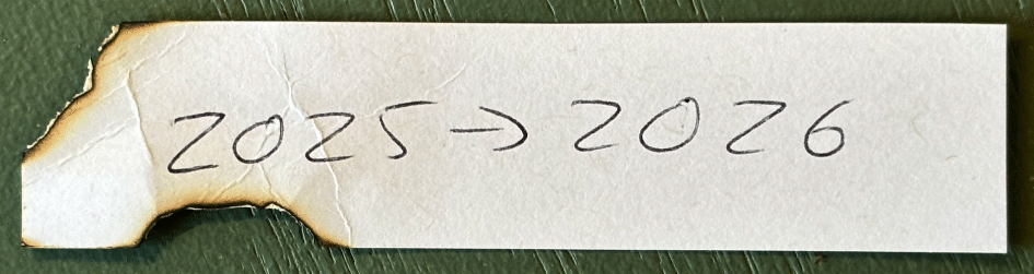 Photo of singed and twisted scrap of paper with 2025 > 2026 written in pen.